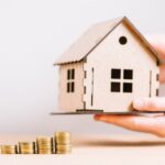 hand holding house near coins